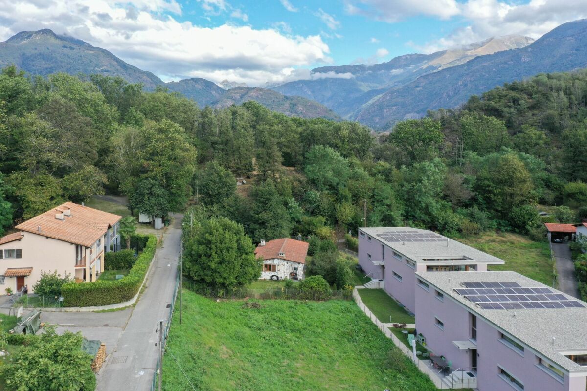 Luftaufnahme eines grünen Tals mit Wohnhäusern und Bergpanorama