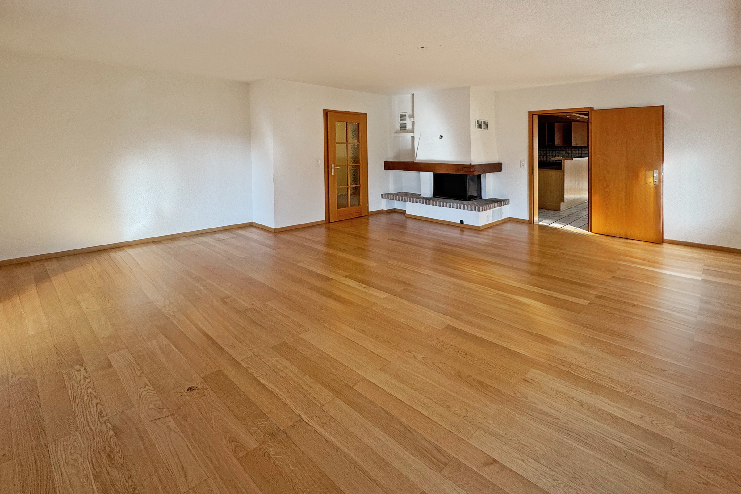 Leerer Wohnraum mit Kamin und Parkettboden