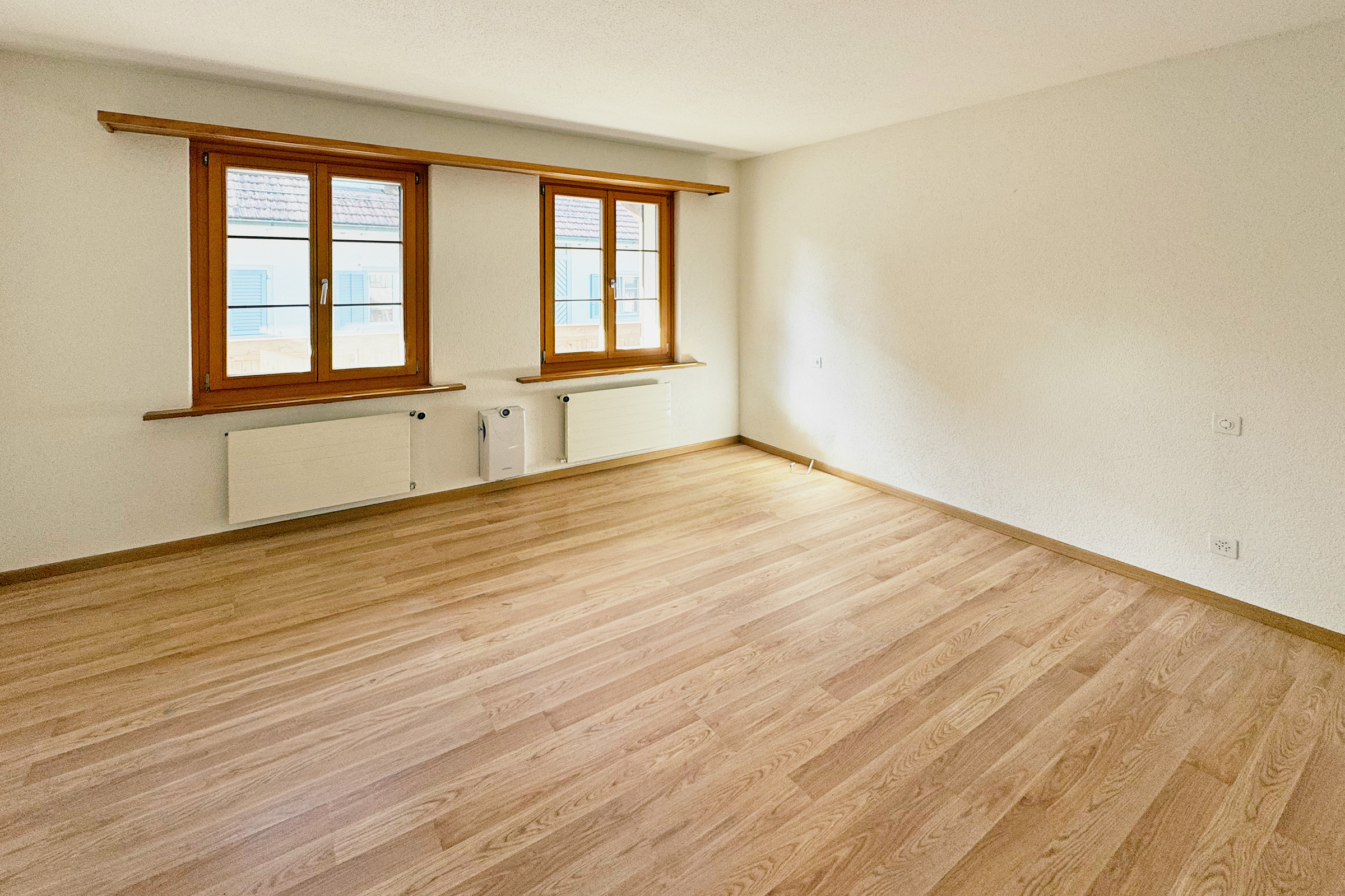 Leeres, helles Zimmer mit Holzfenstern und Parkettboden
