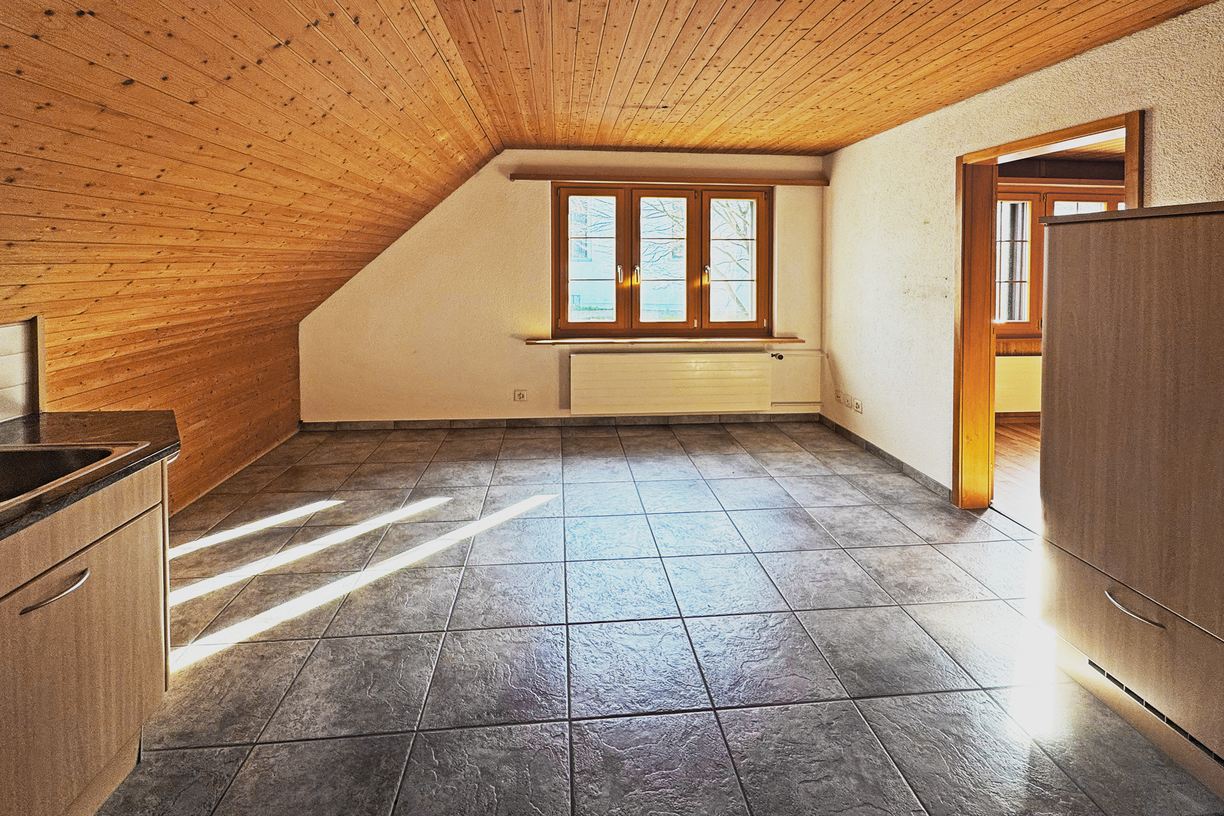 Leerer Dachgeschossraum mit Holzdecke und Fliesenboden