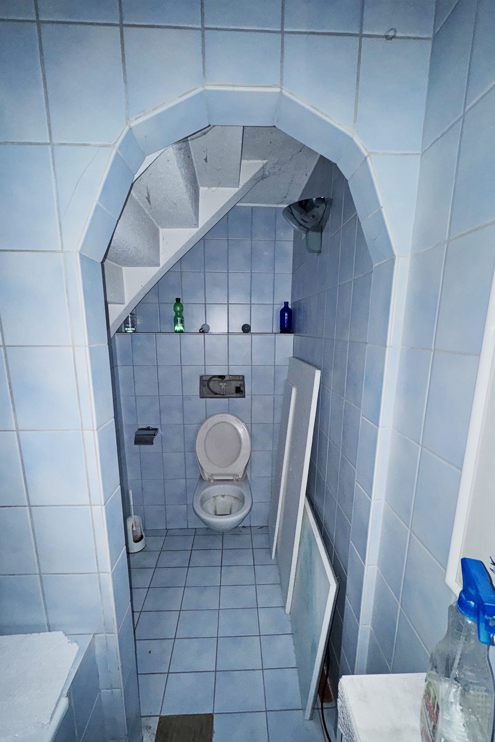 Kleines blau gefliestes WC unter einer Treppe