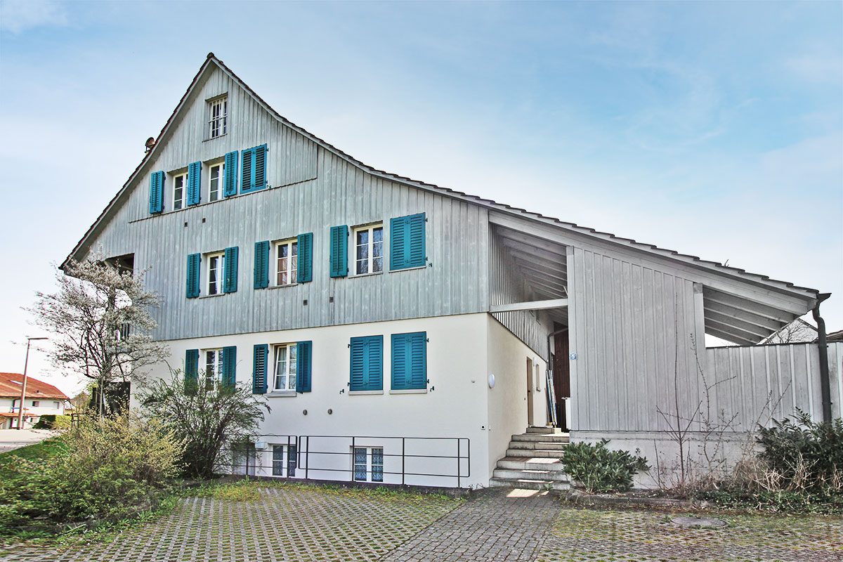 Außenansicht eines Hauses mit Holzfassade und blauen Fensterläden