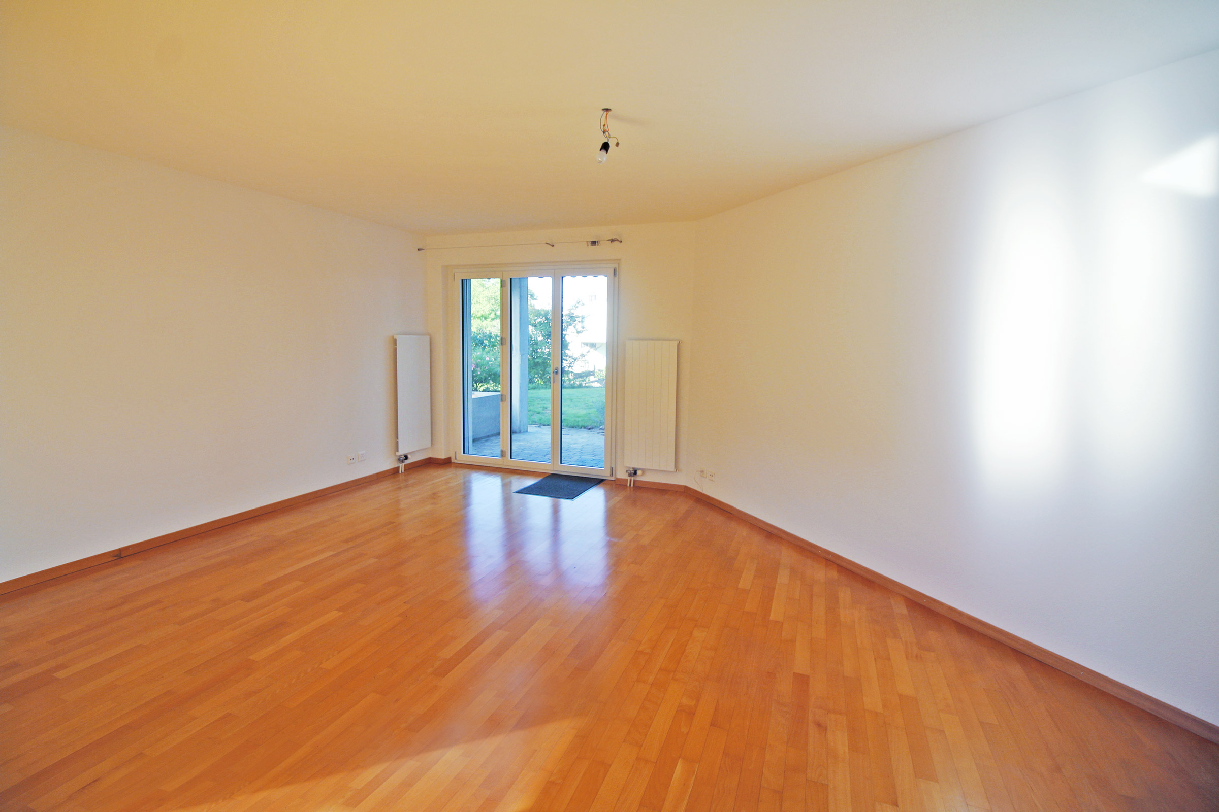 Leerer Wohnraum mit Holzboden und Terrassentür