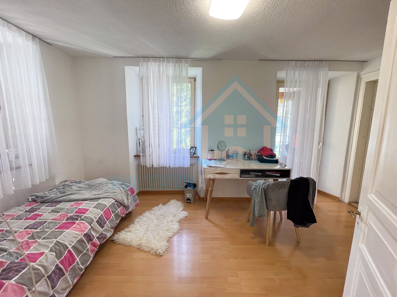 Helles Schlafzimmer mit Bett, Schreibtisch und zwei Fenstern