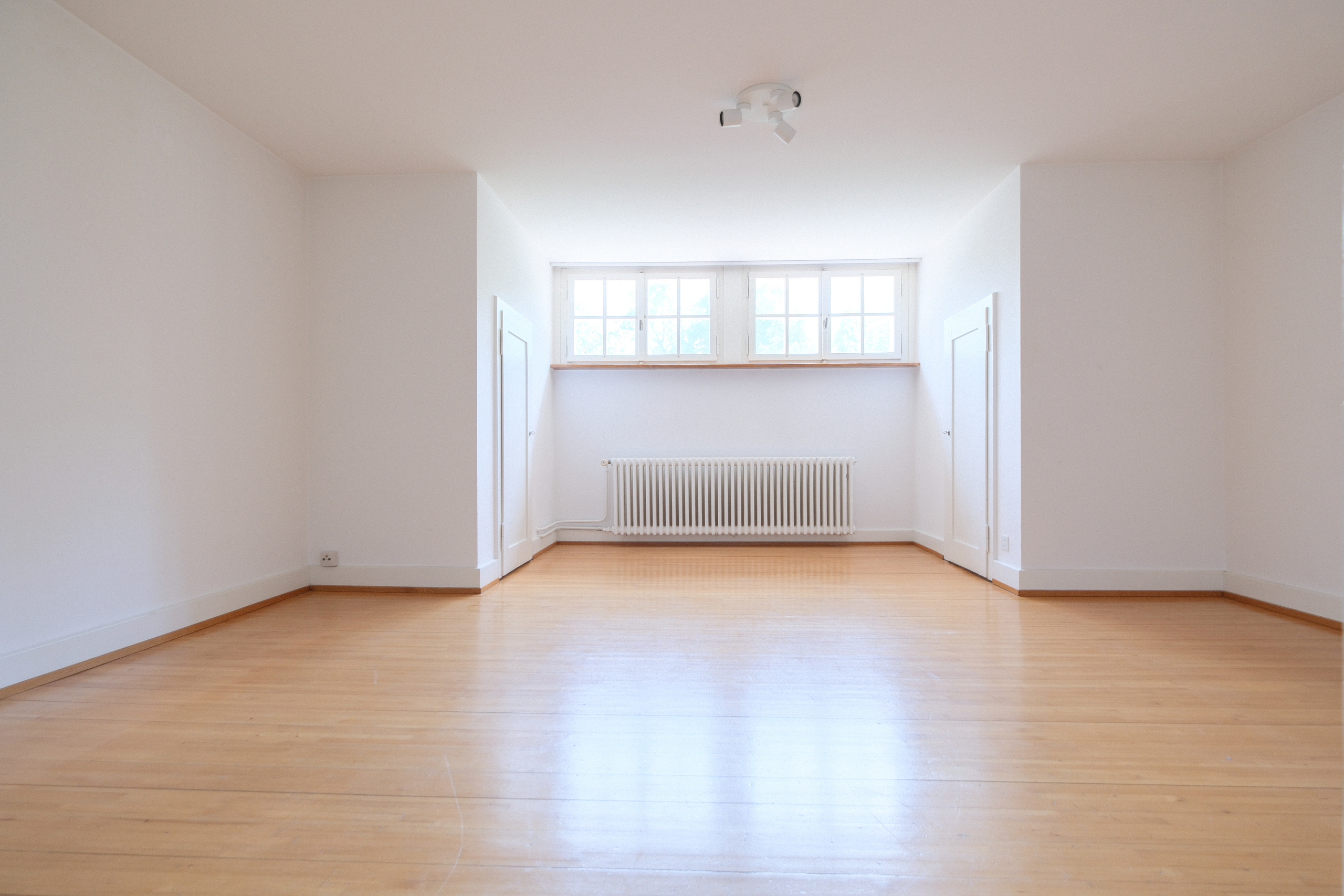 Heller leerer Raum mit Holzfußboden und zentralem Fensterband