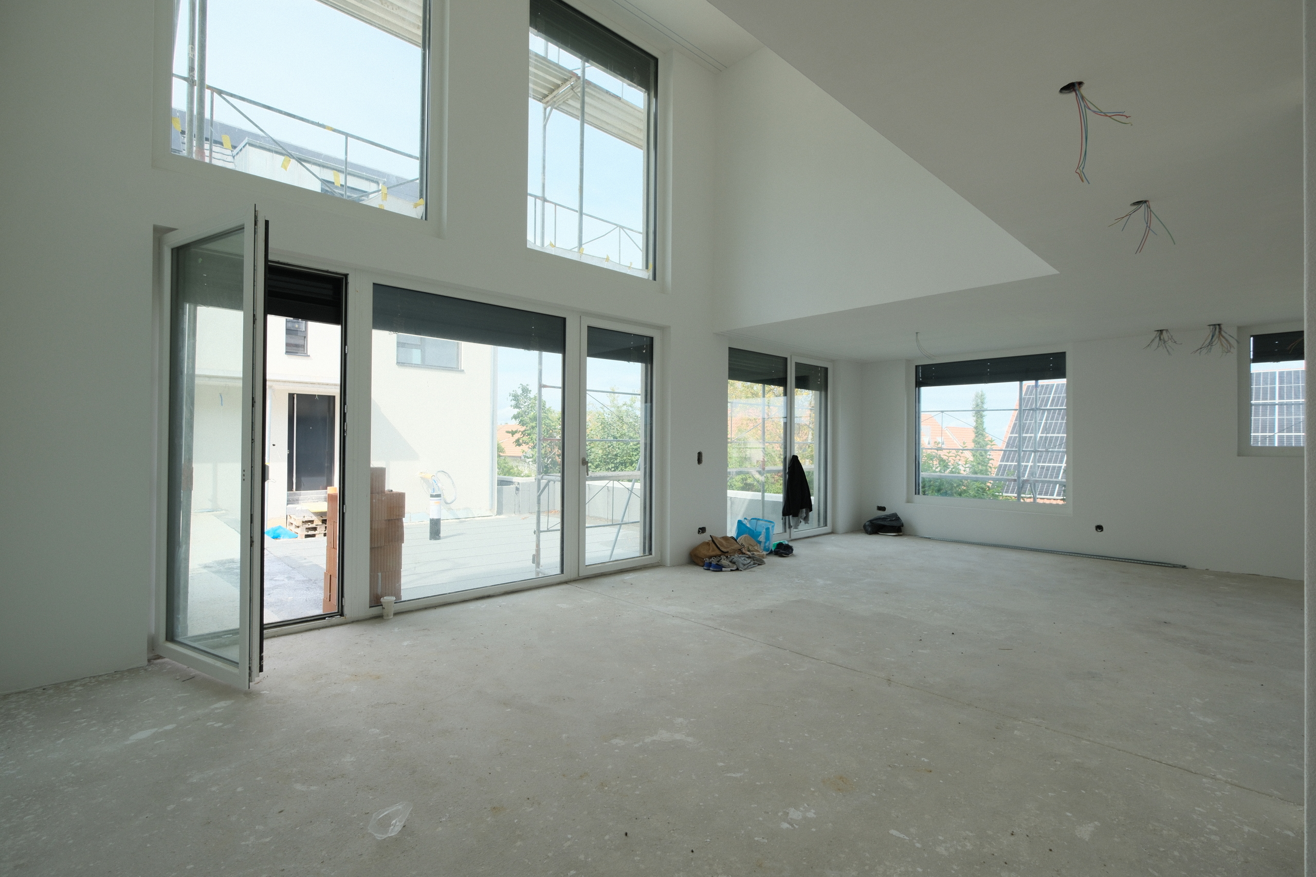 Großer, leerer Wohnraum im Rohbau mit hohen Fenstern