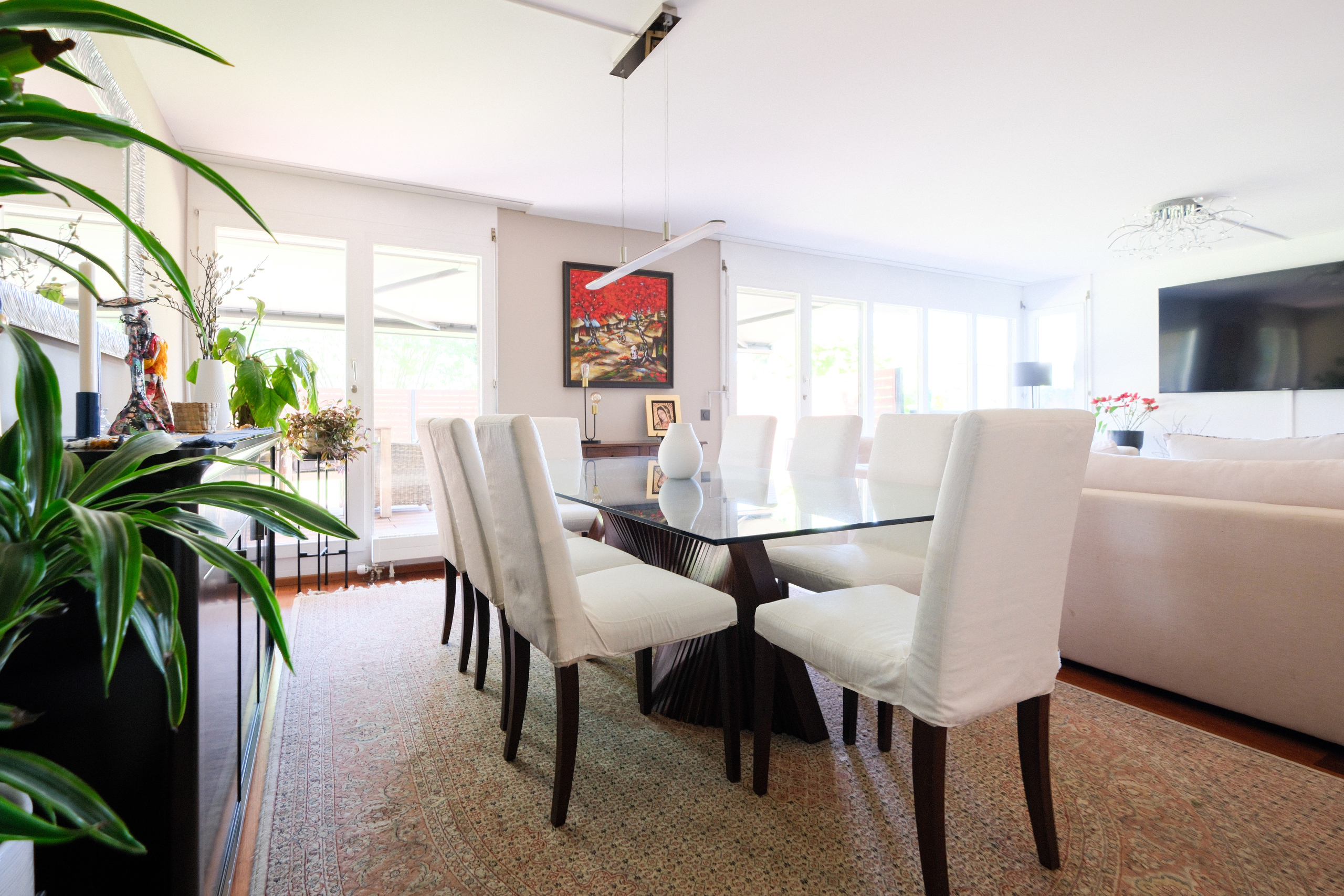 Helles Esszimmer mit Glas­tisch und weißen Stühlen