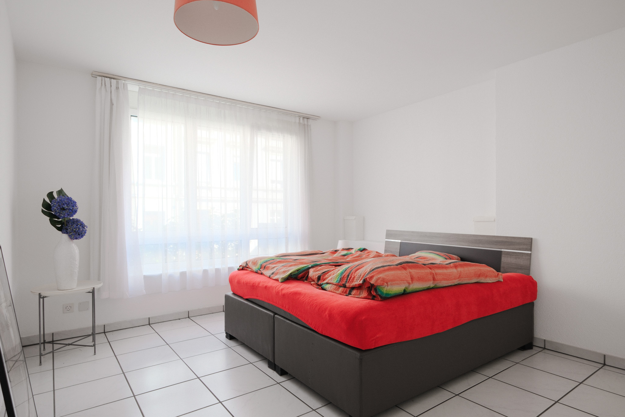 Helles Schlafzimmer mit großem Fenster und roter Bettwäsche