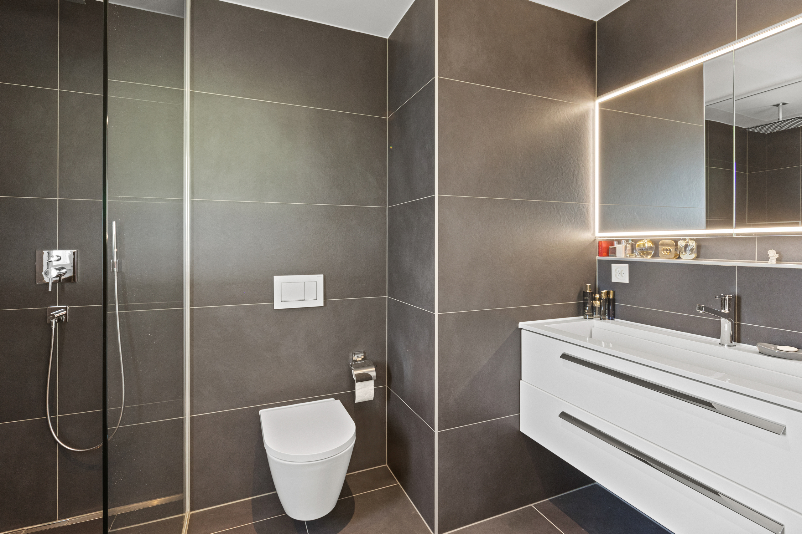 Modernes Badezimmer mit dunkler Wandverkleidung und beleuchtetem Spiegel