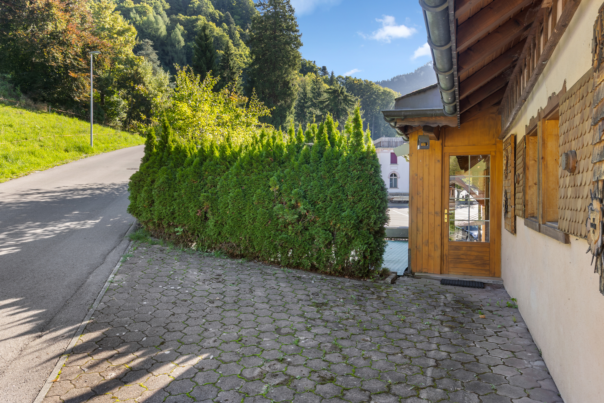 Außenansicht eines alpenländischen Gebäudes mit Zufahrt und Gartenrand