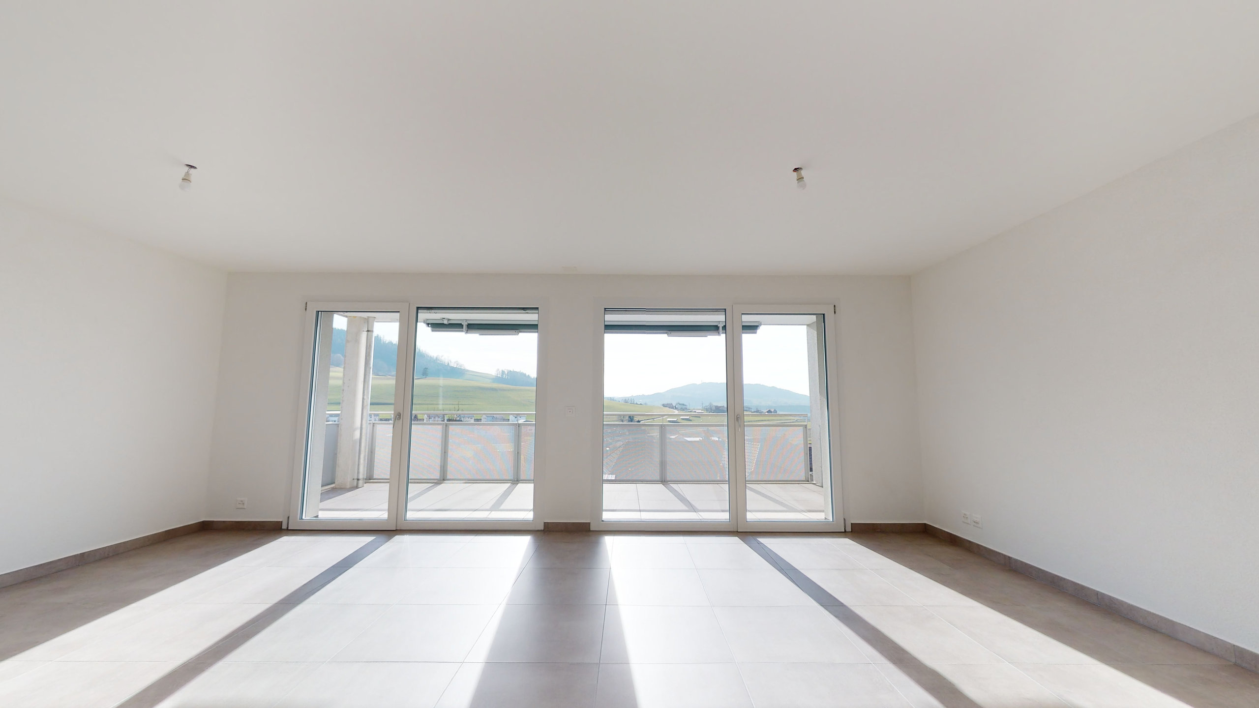 Leerer, heller Wohnraum mit Balkon und Fernblick