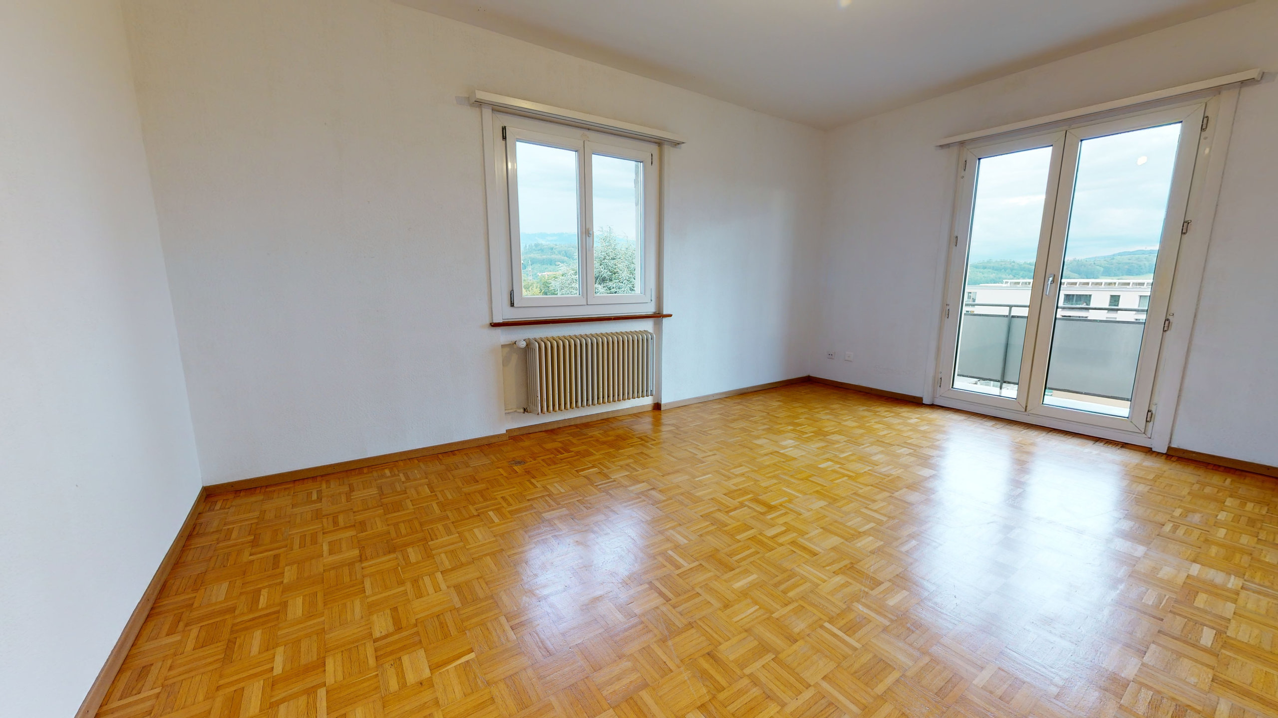 Leerer Wohnraum mit Balkon und Parkettboden