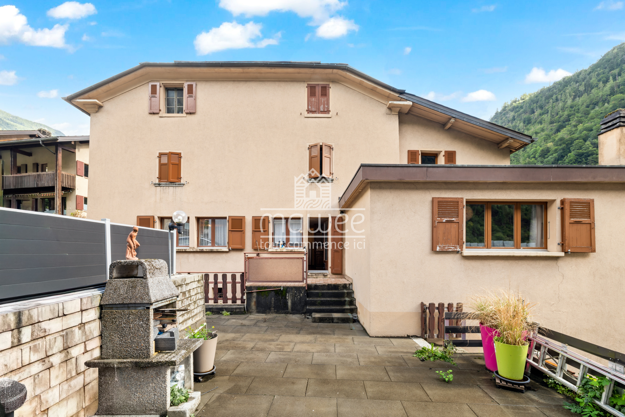 Beige Haus mit Holzfensterläden und Bergkulisse