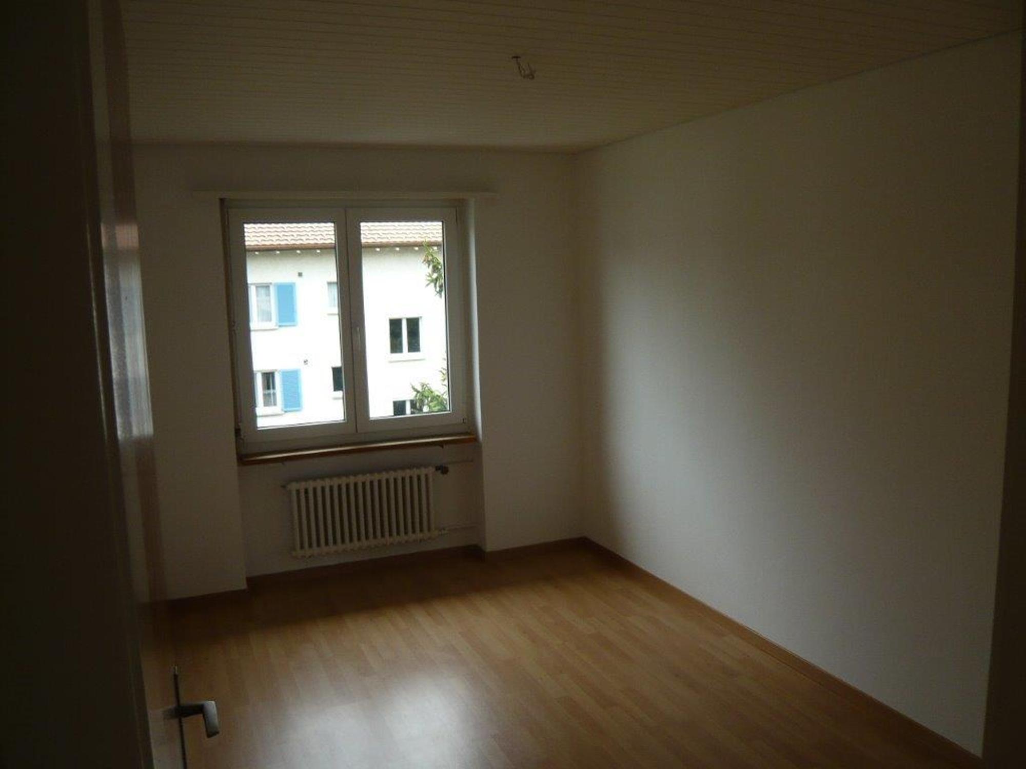 Leeres, schlichtes Zimmer mit Fenster und Heizkörper