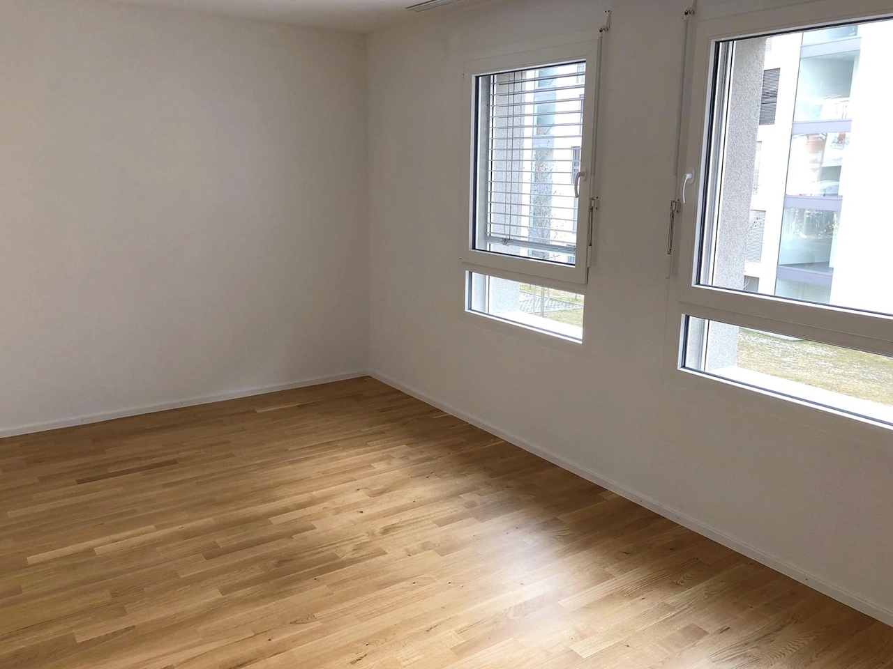 Heller leerer Raum mit Holzboden und großen Fenstern