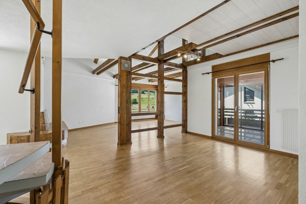 Großer leerer Wohnraum mit Holzbalken und Balkonzugang