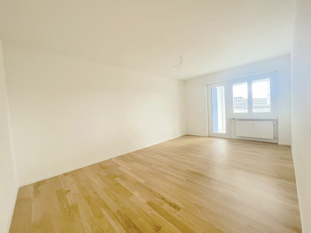 Heller leerer Wohnraum mit Holzfußboden und Balkonfenster