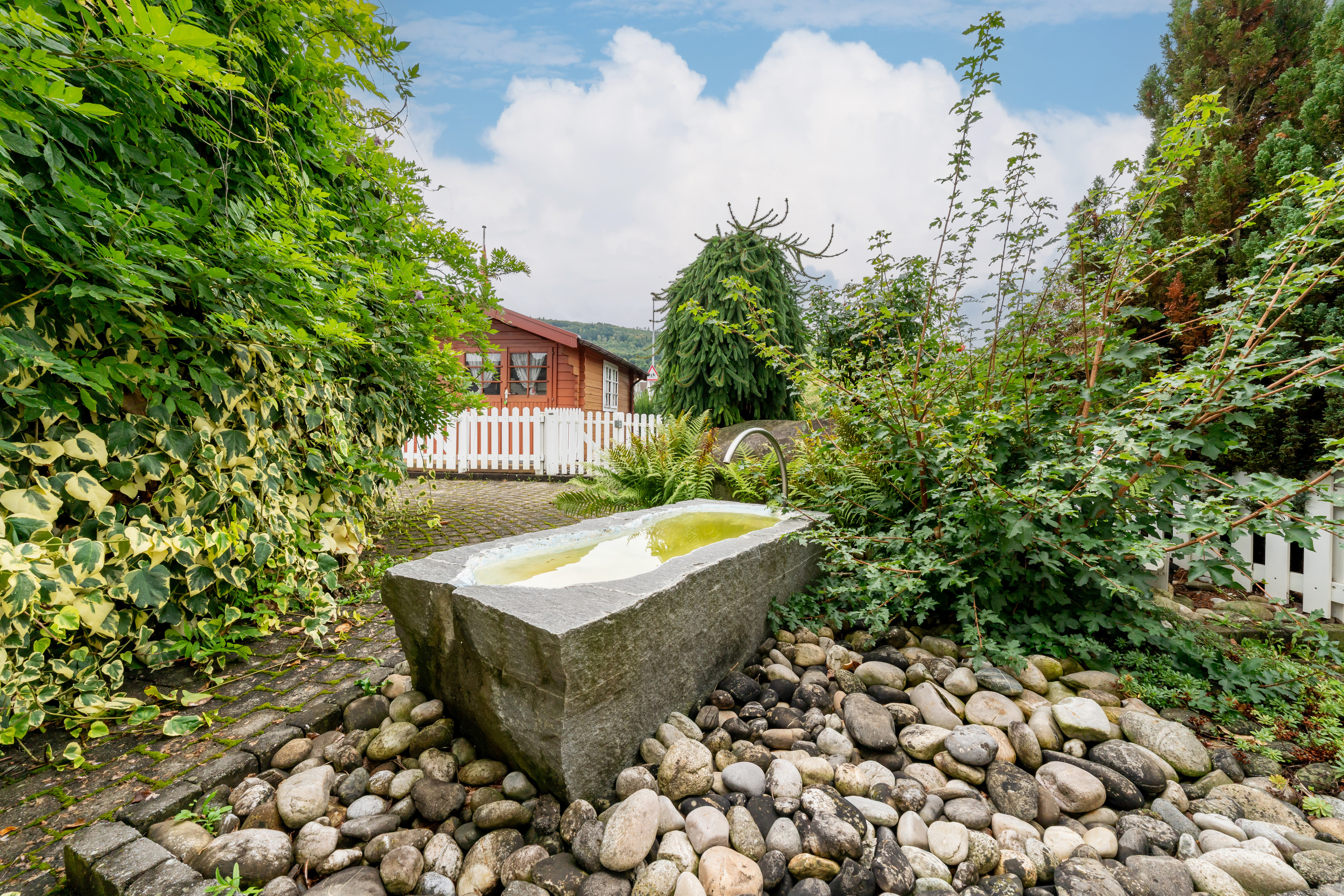 Garten mit Natursteinbecken und Holzhütte