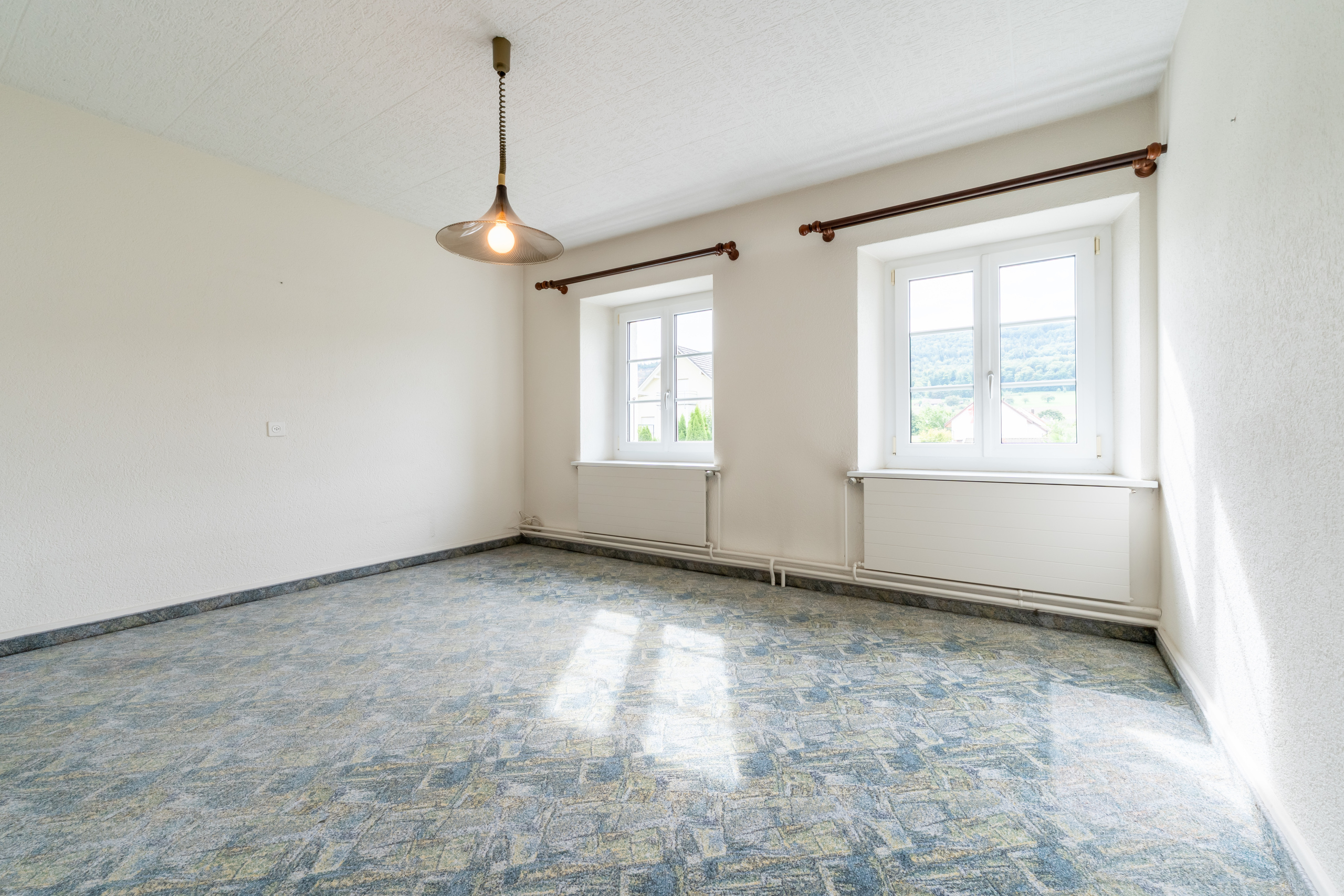Leerer heller Raum mit zwei Fenstern und gemustertem Teppichboden
