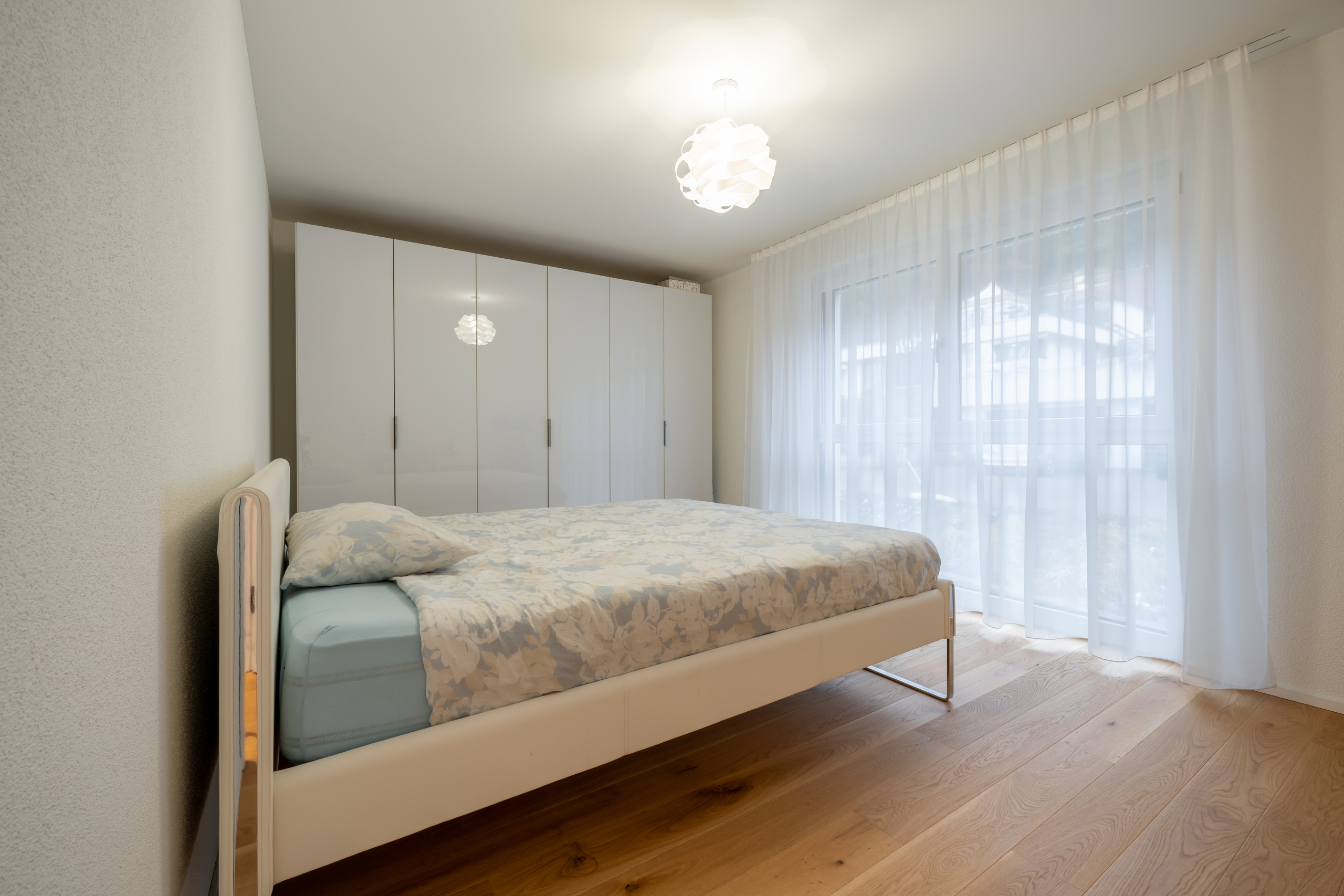 Helles Schlafzimmer mit Schrankwand und Tageslichtvorhängen