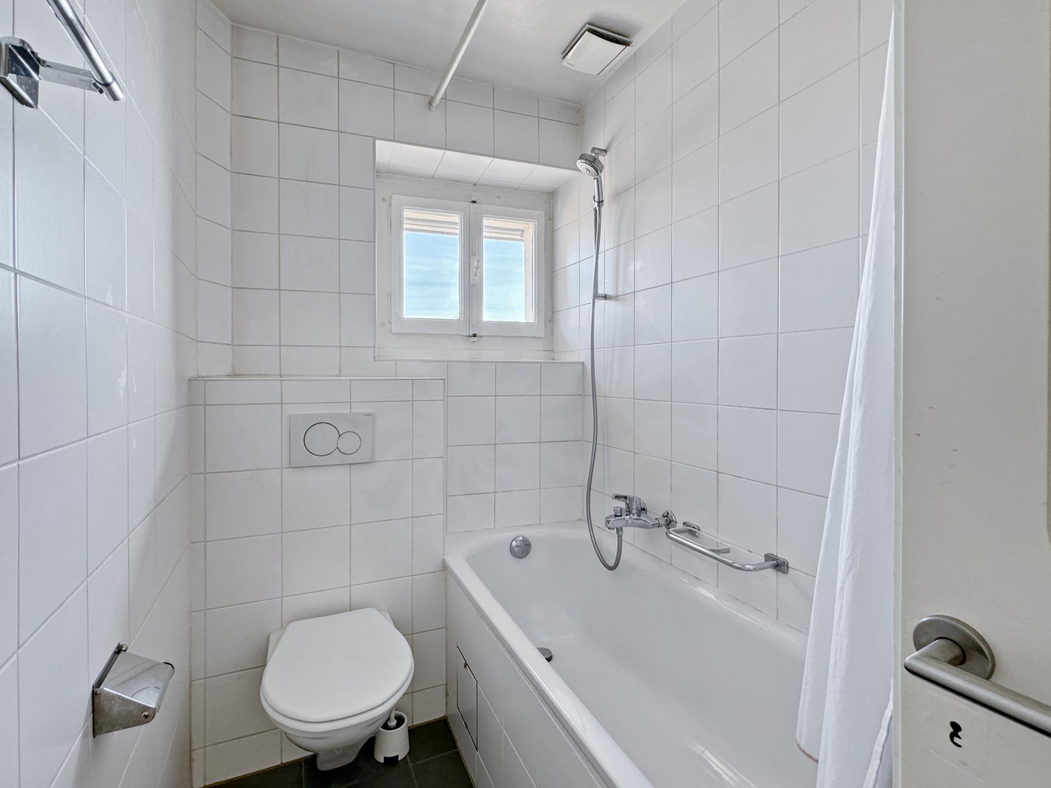 Kleines weiß gefliestes Badezimmer mit Badewanne und Toilette