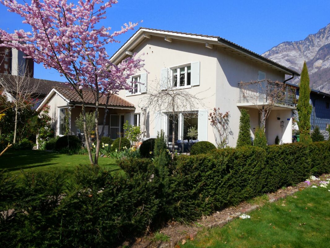 Einfamilienhaus mit blühendem Garten und Bergkulisse