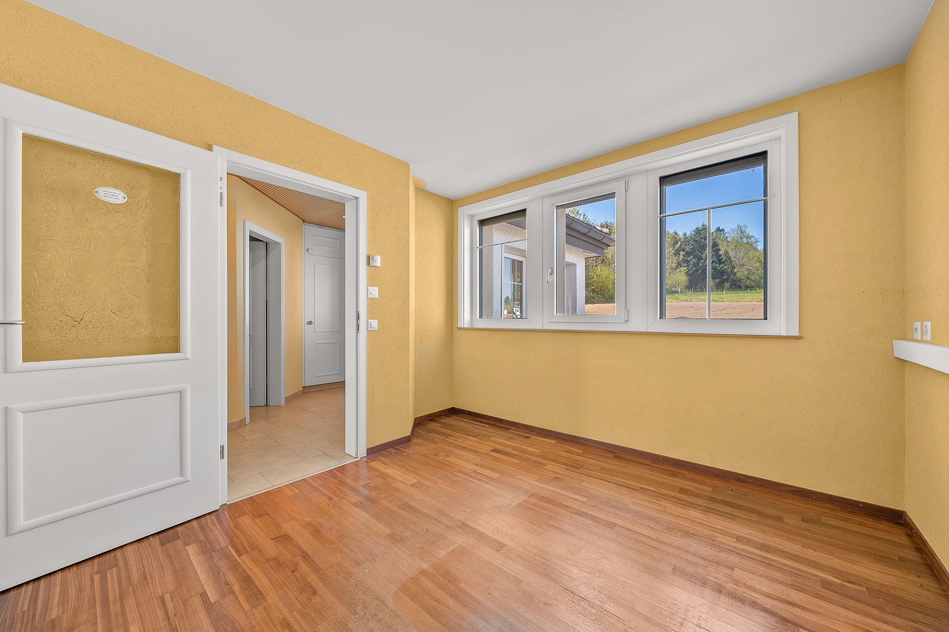 Helles Zimmer mit Holzoptik-Boden und Fenstern