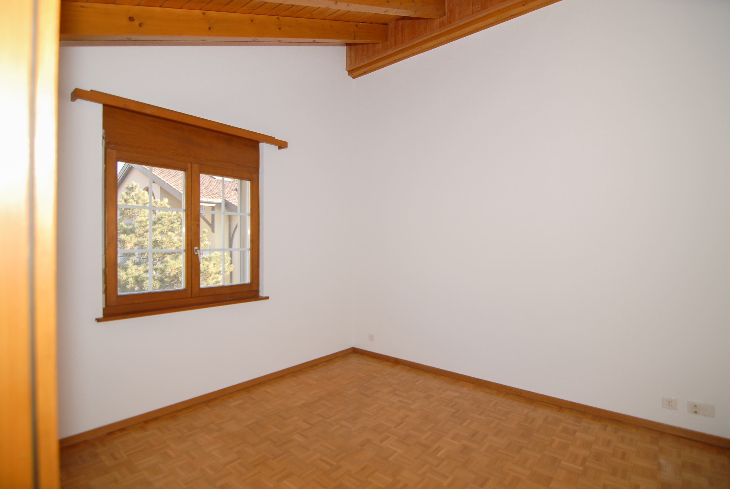 Leeres Zimmer mit Holzfenster und sichtbaren Deckenbalken