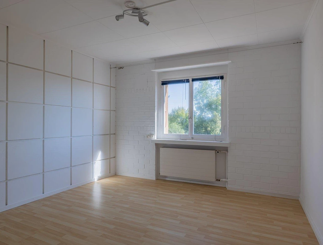 Helles, leeres Zimmer mit Fenster und Holzoptikboden