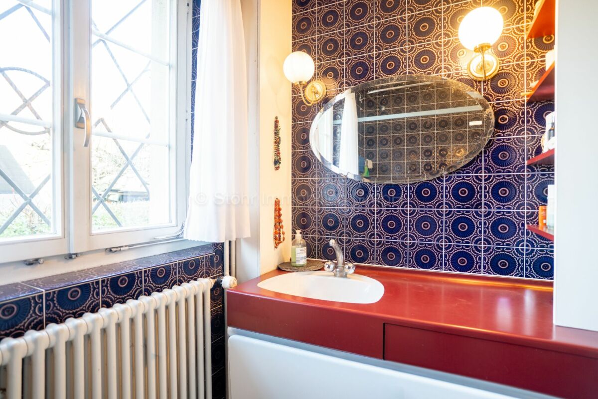 Badezimmer mit gemusterten Fliesen und rotem Waschtisch