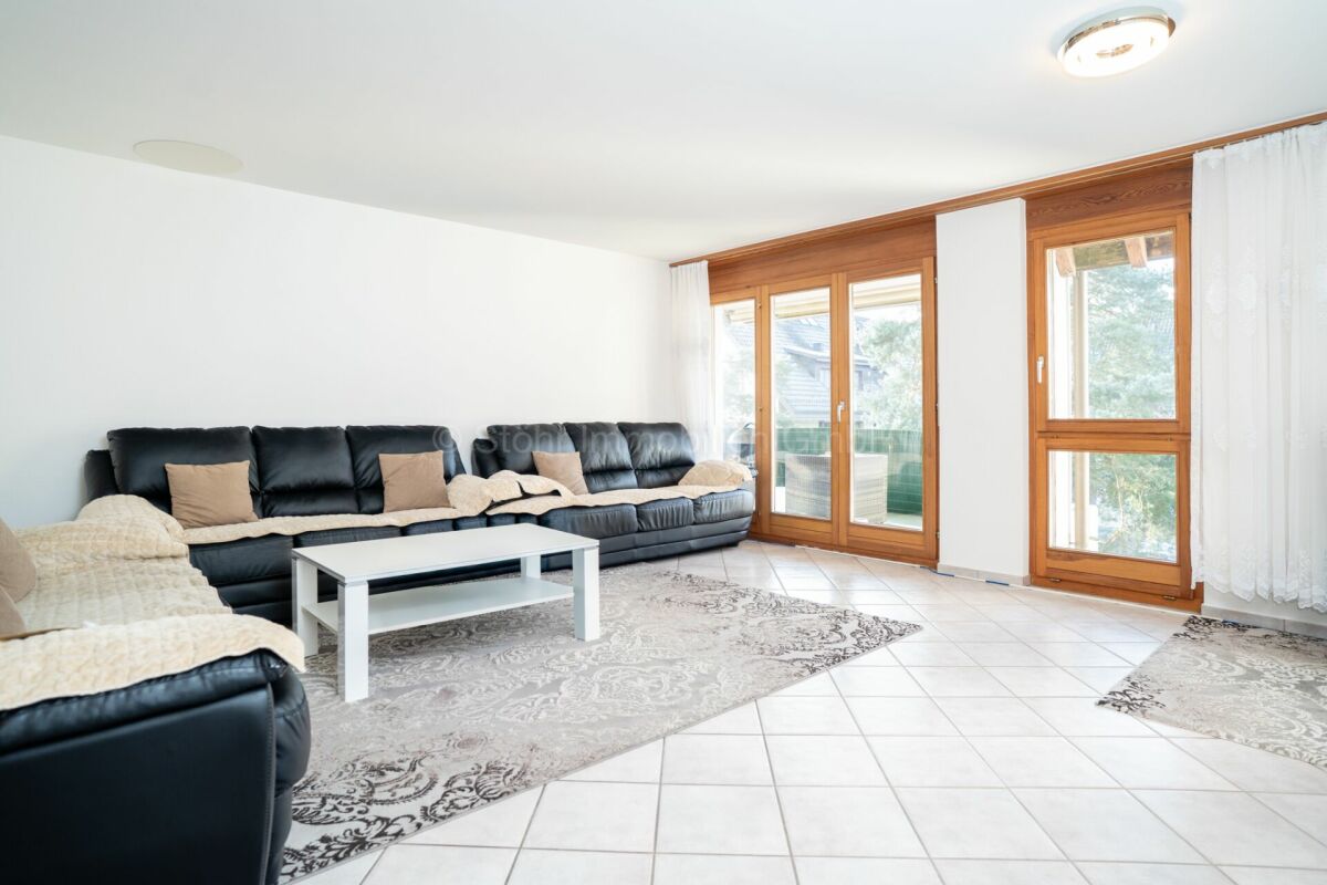 Helles Wohnzimmer mit bodentiefen Holzfenstern und großer Sitzgruppe