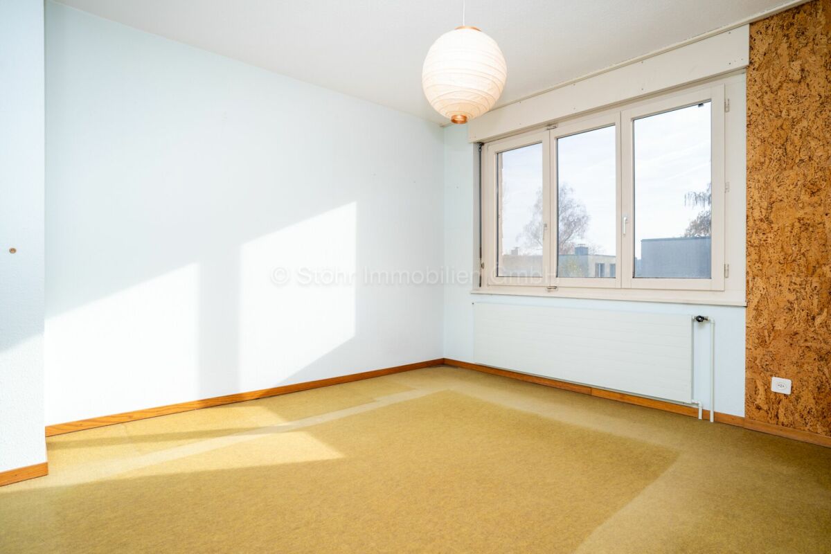 Helles, leeres Zimmer mit großem Fenster und Teppichboden