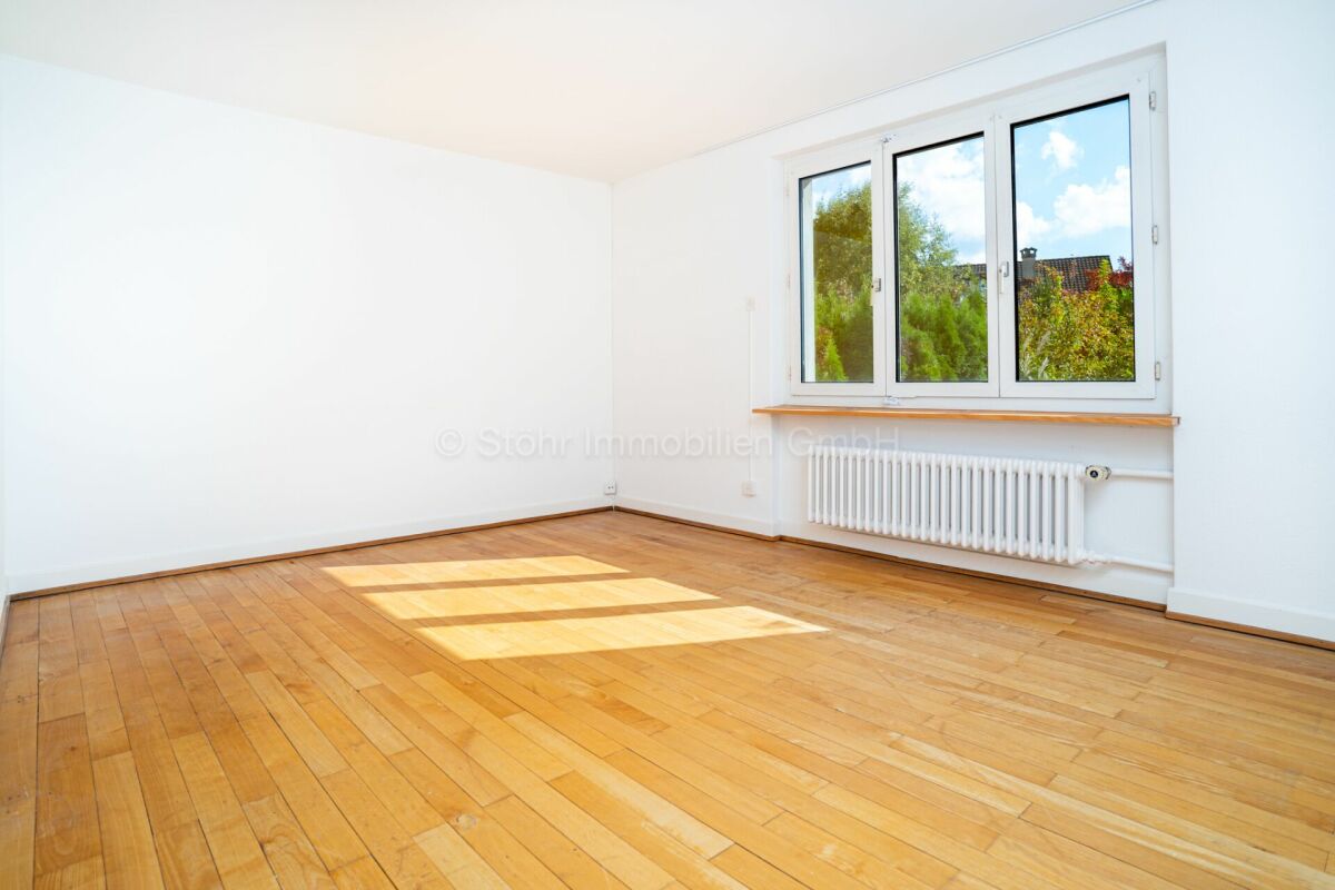 Helles, leeres Zimmer mit Holzboden und Fenster