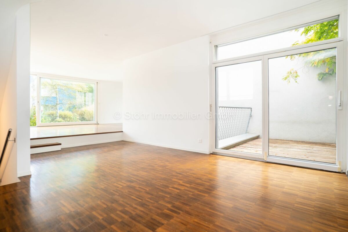 Heller, leerer Wohnraum mit Holzfußboden und Balkonzugang