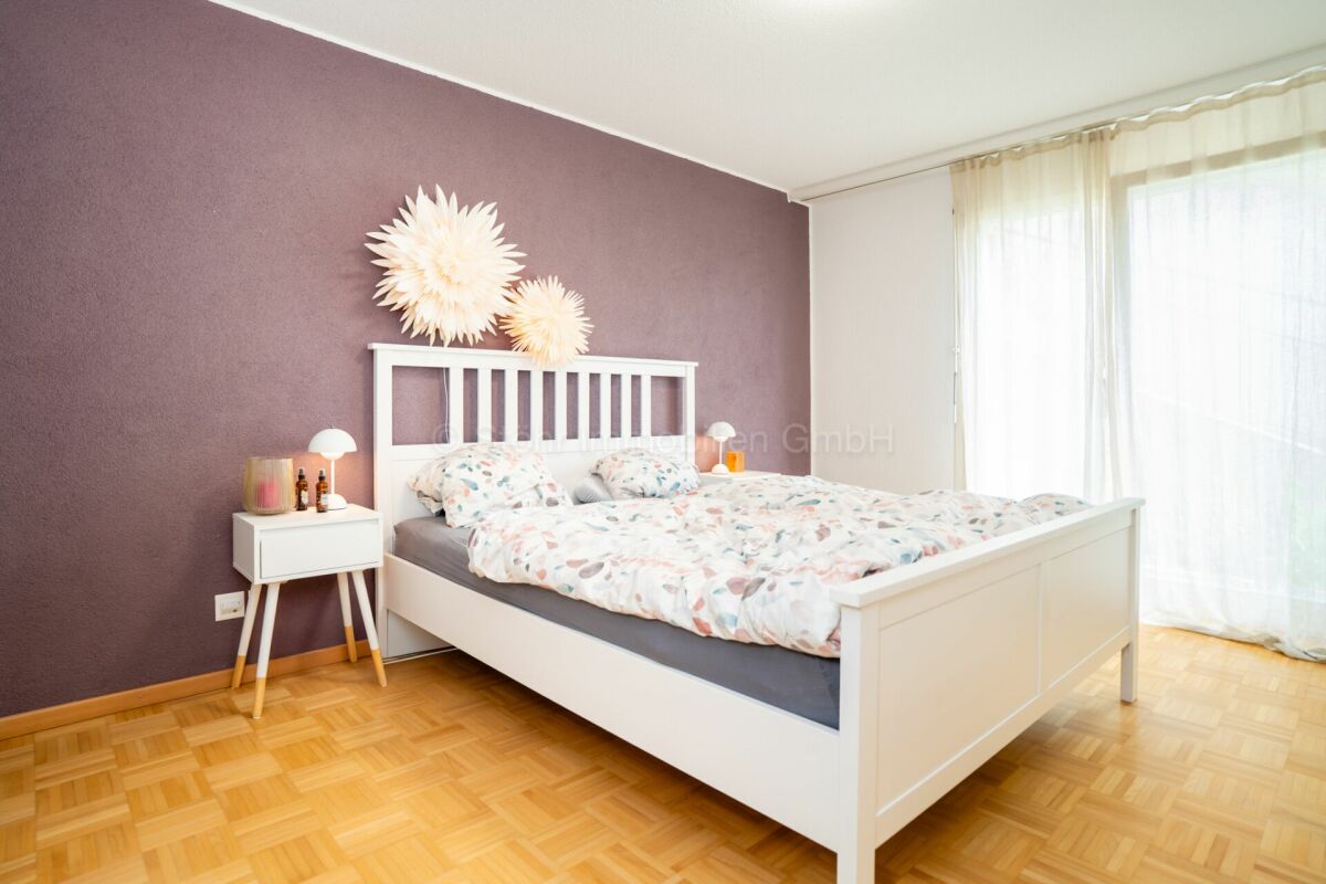Helles Schlafzimmer mit weißem Bett und violetter Akzentwand