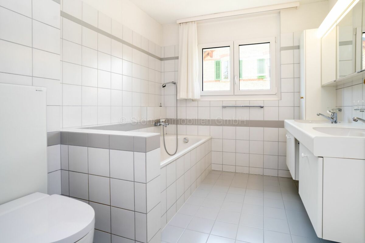 Helles, weiß gefliestes Badezimmer mit Badewanne und Waschtisch