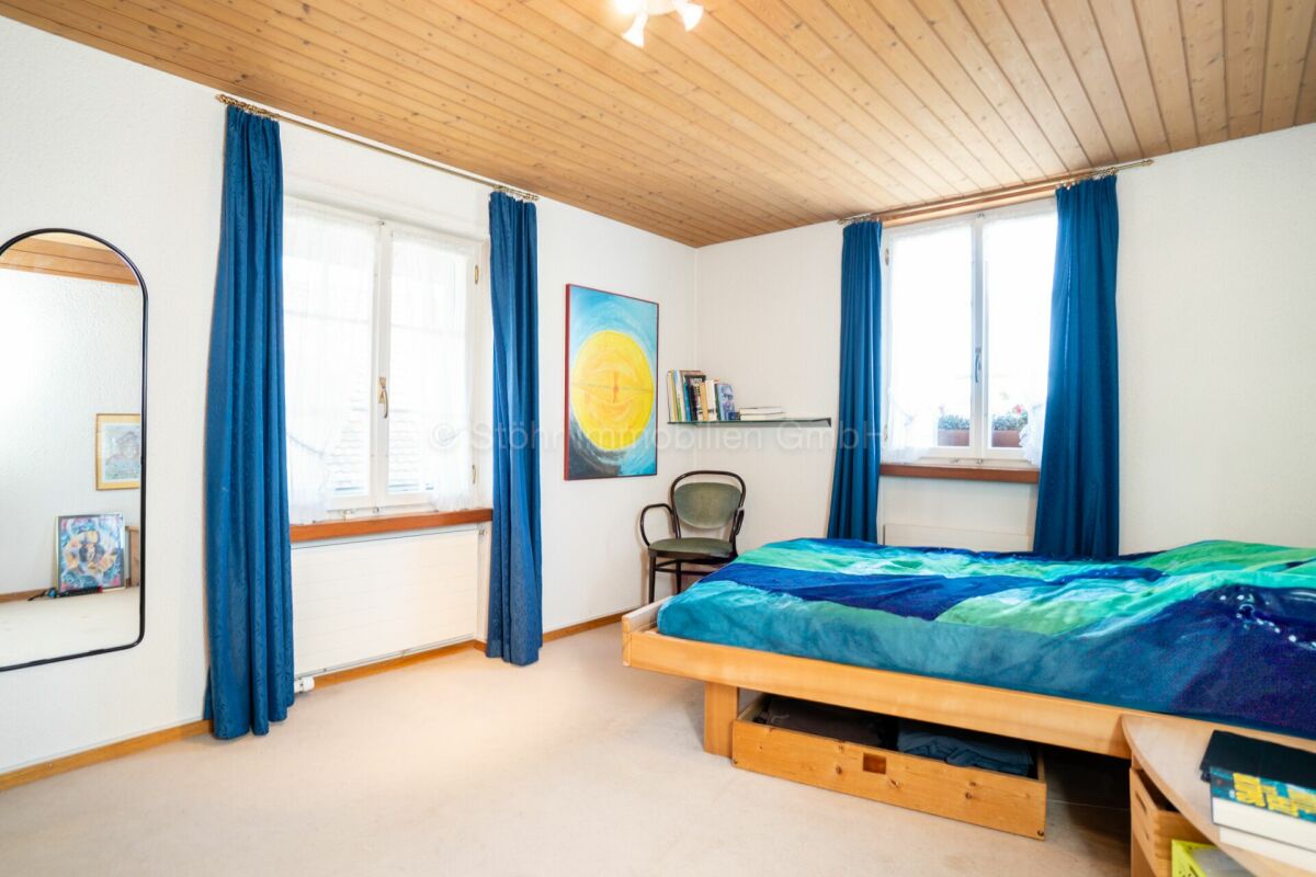 Helles Schlafzimmer mit Holzdecke und blauen Vorhängen