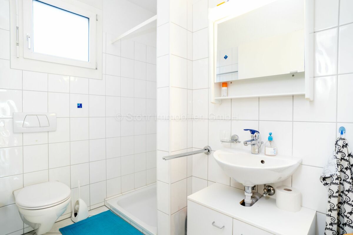 Kleines weiß gefliestes Badezimmer mit WC, Waschbecken und Fenster