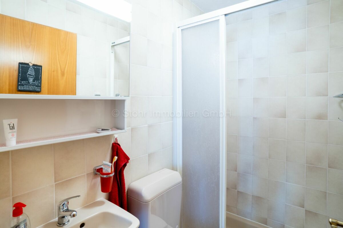 Kleines weiß gefliestes Badezimmer mit Dusche und Waschtisch