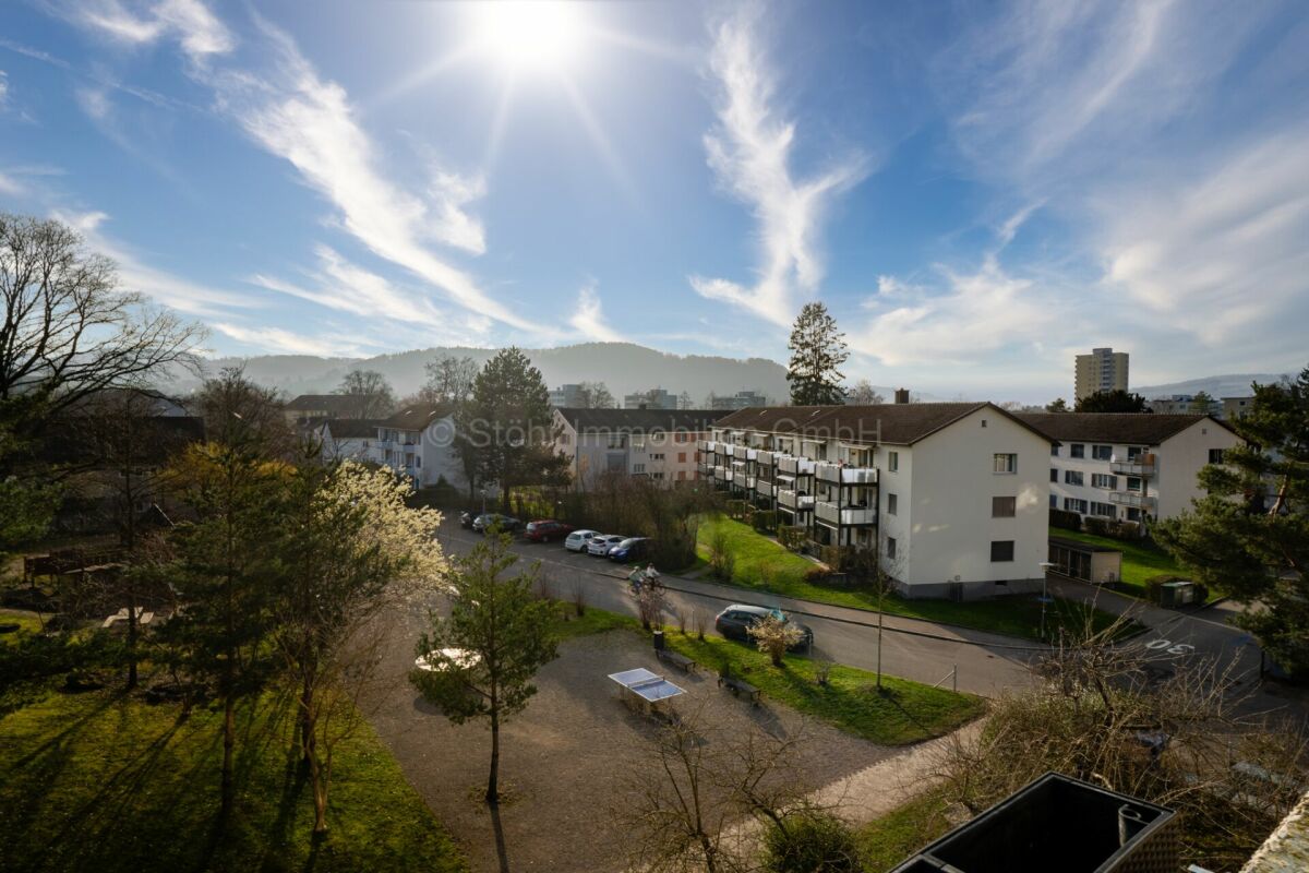 Blick über eine Wohnanlage mit Grünflächen und Bergen im Hintergrund