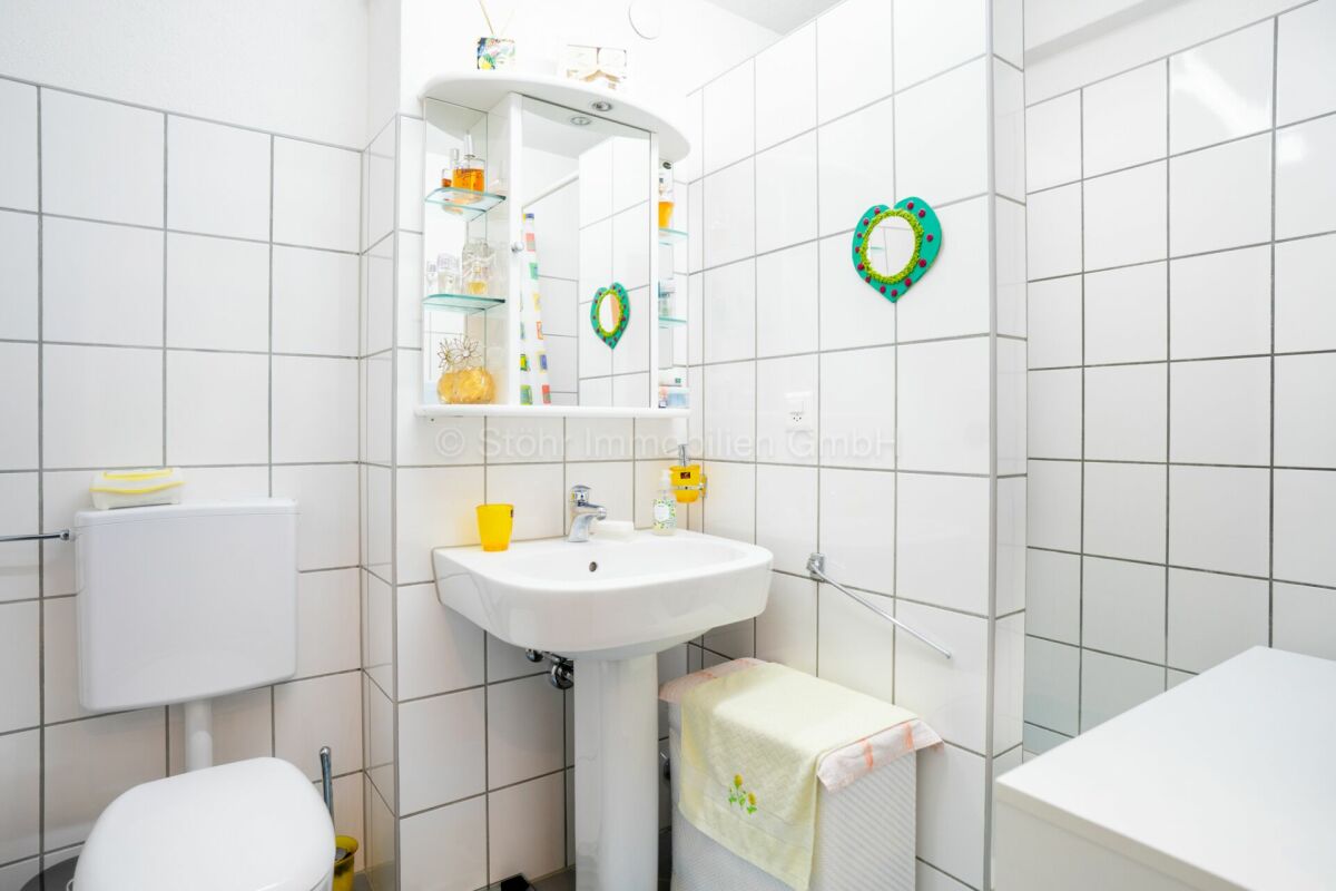 Kleines weiß gefliestes Badezimmer mit Waschbecken und WC
