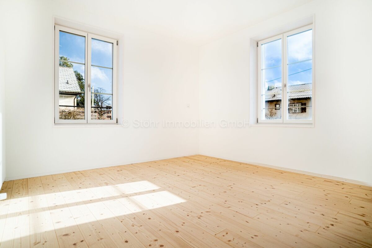 Heller, leerer Raum mit zwei Fenstern und Holzboden