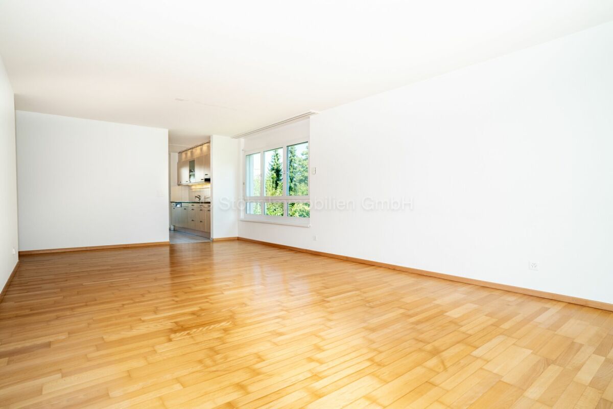 Heller leerer Wohnraum mit Holzboden und Blick zur Küche