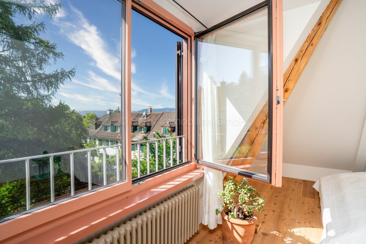 Dachgeschosszimmer mit offenem Fenster und Balkonblick