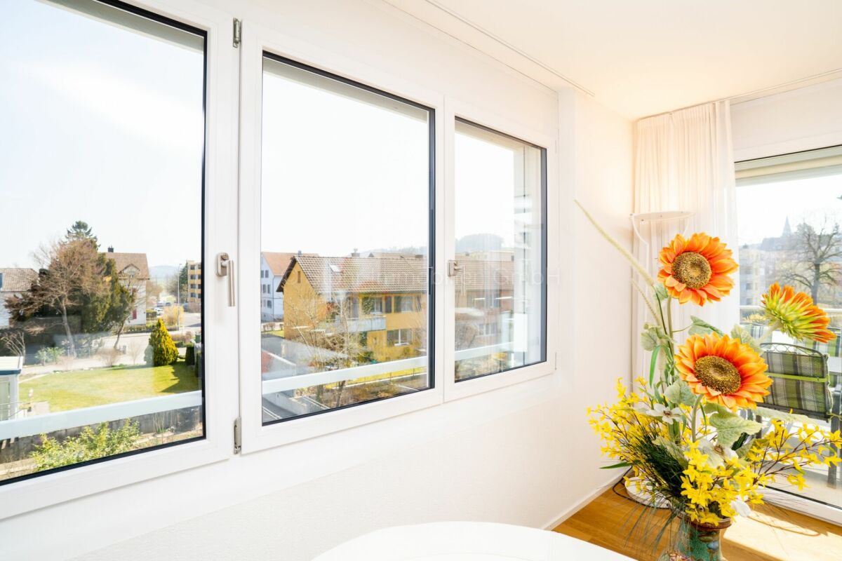 Helles Zimmer mit großen Fenstern und Blumenarrangement