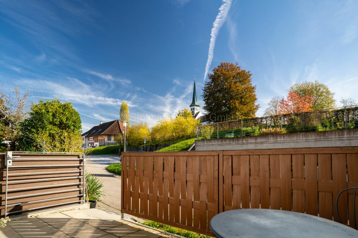Blick auf einen begrünten Außenbereich mit Zaun und Kirchturm