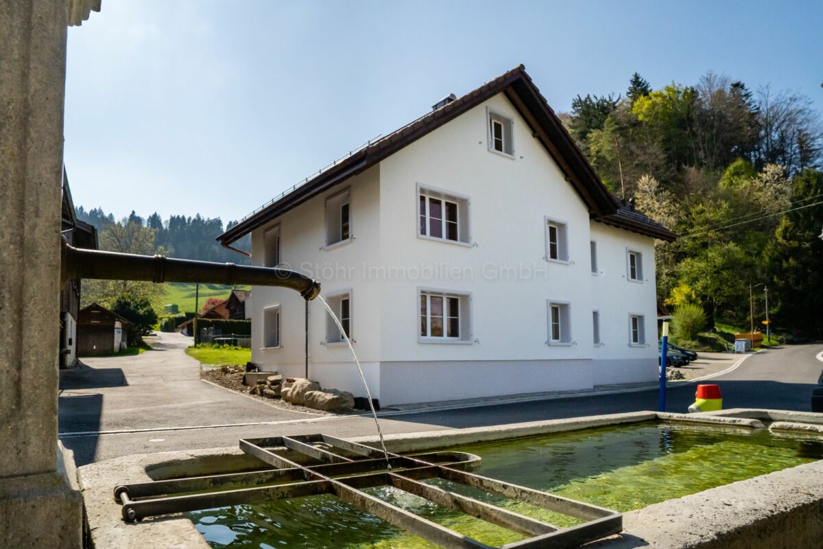 Weißes Wohnhaus mit Brunnen im Vordergrund