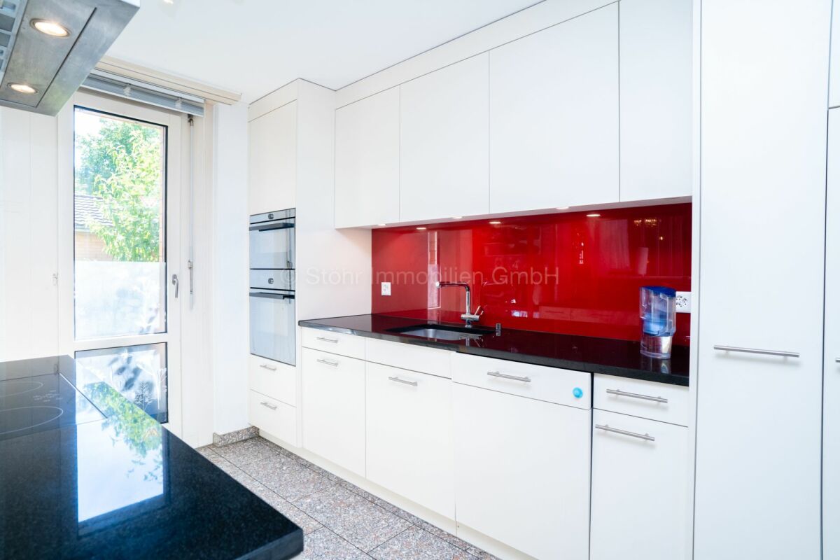 Moderne weiße Küche mit roter Glasrückwand