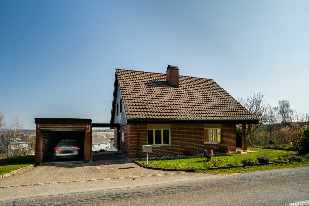 Ein Einfamilienhaus mit Garage und Satteldach am Straßenrand