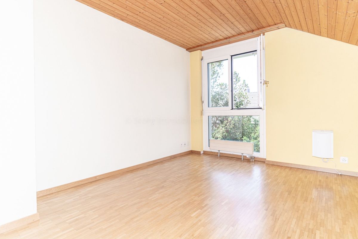 Heller leerer Wohnraum mit Holzdecke und großem Fenster